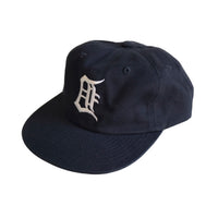 Angled view of navy blue cap showing white embroidered backwards “D” on the front panel.