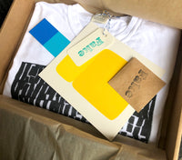 Inside the kraft EK box: folded tee, colorful inserts, a pin, and branding materials tucked in tissue wrap.