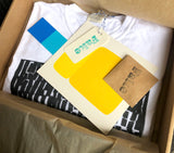 Inside the kraft EK box: folded tee, colorful inserts, a pin, and branding materials tucked in tissue wrap.